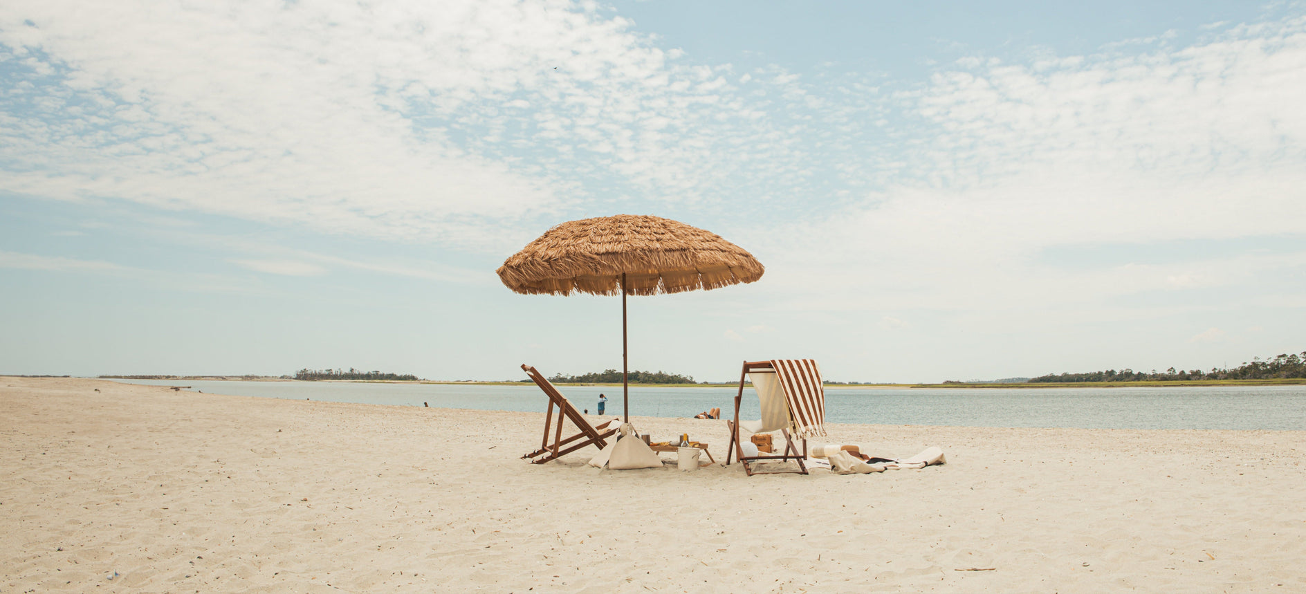 Beach scene with a natural umbrella and lounge chairs under a blue sky with clouds.