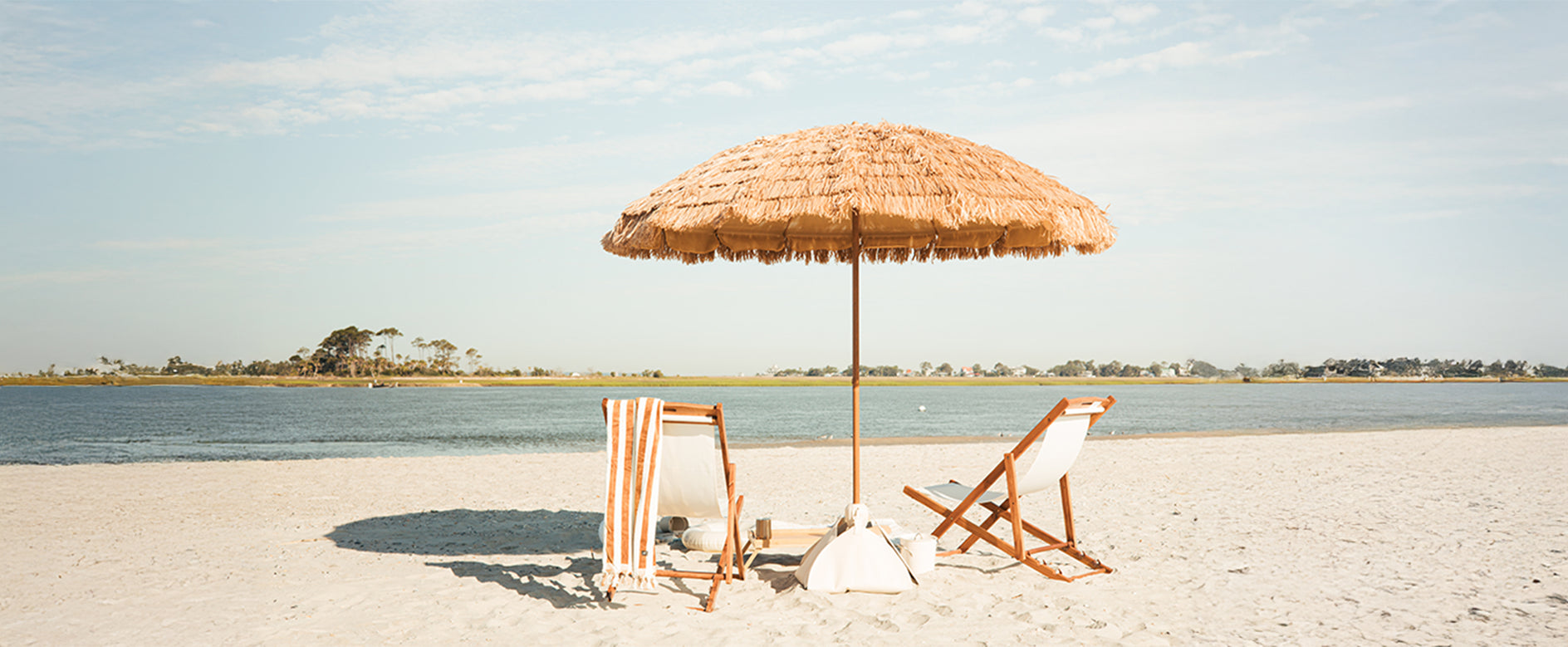 The Sirocco - Natural beach umbrella and lounge chairs on a sandy shore.