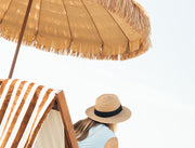 Women wearing a straw hat under a Natural umbrella on a beach.