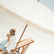 Woman sitting under a large luxury beige umbrella on a beach.