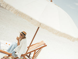 Woman sitting under a large luxury beige umbrella on a beach.