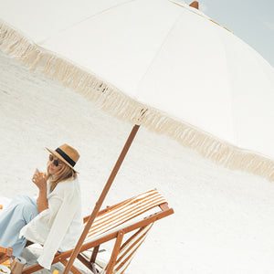 Woman sitting under a large luxury beige umbrella on a beach.