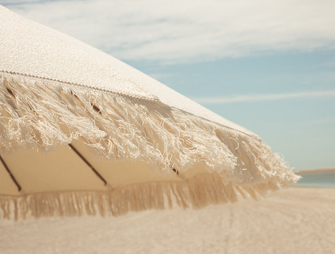Beige umbrella with tassels against a clear blue sky