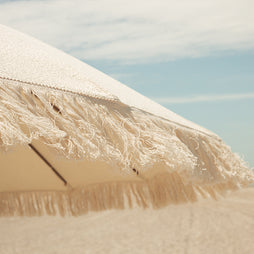 Beige umbrella with tassels against a clear blue sky