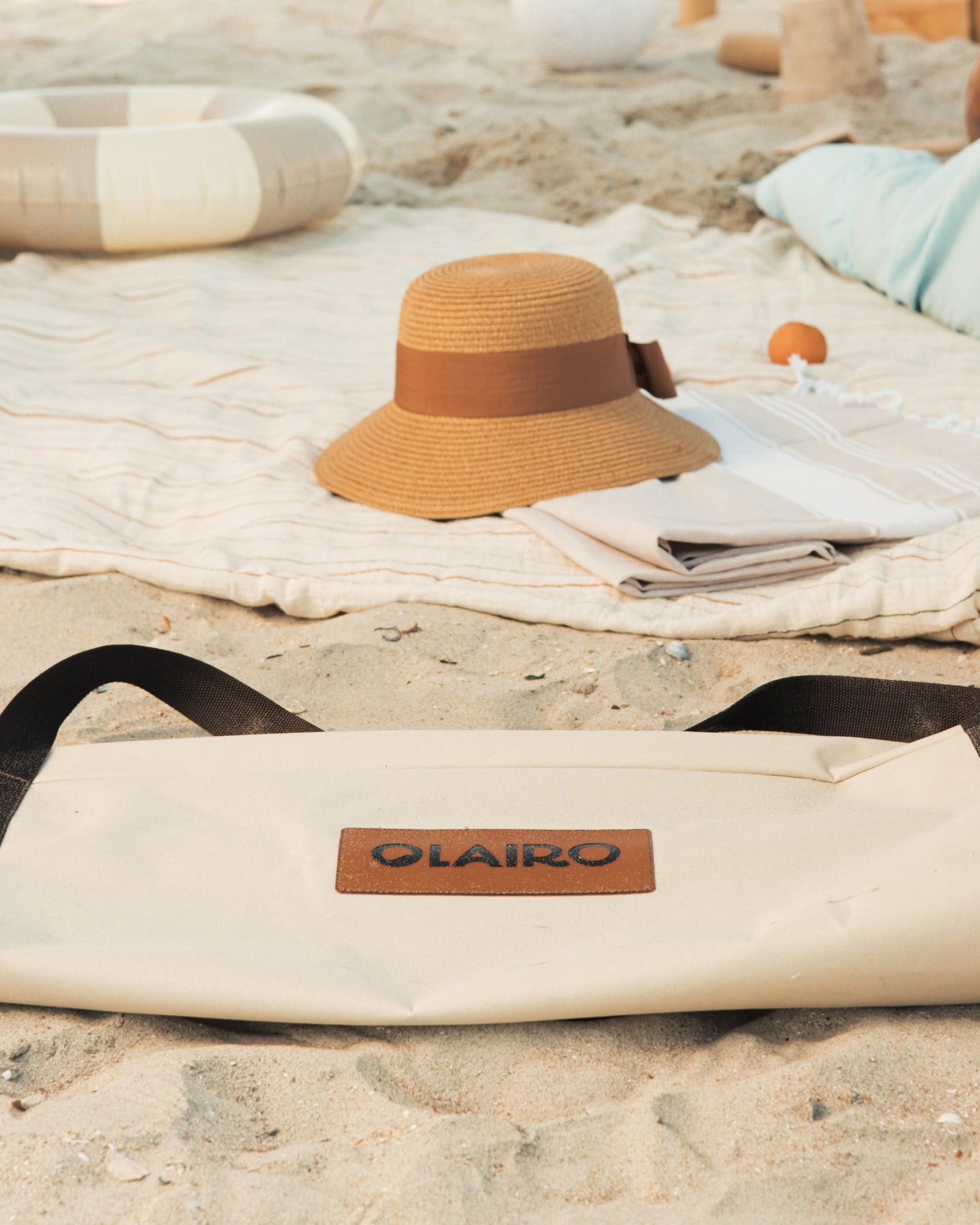 Olairo brand logo on a canvas umbrella carry bag on a sandy beach with a sun hat and towel.